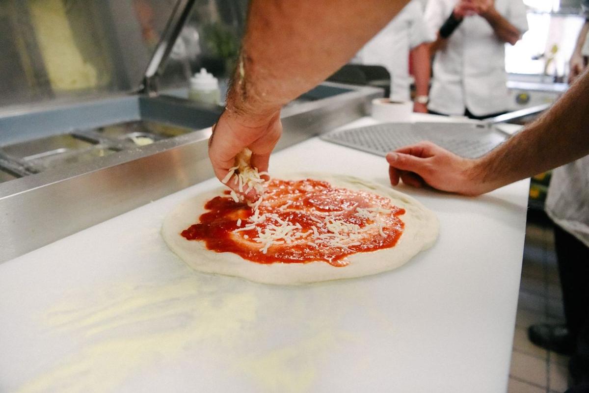 Saucing and topping a fresh-stretched pie in the kitchen